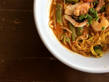 Delicious asian spicy seafood noodle soup with shrimp, squid and shellfish in white bowl on wooden table, Tom Yum Goong. Thai style food. vintage tone color filter.の写真素材