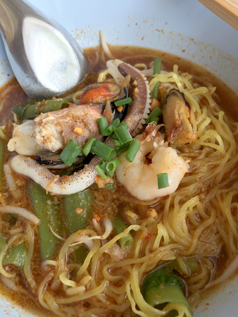 Delicious asian spicy seafood noodle soup with shrimp, squid and shellfish in white bowl on wooden table, Tom Yum Goong. Thai style food. vintage tone color filter.の写真素材
