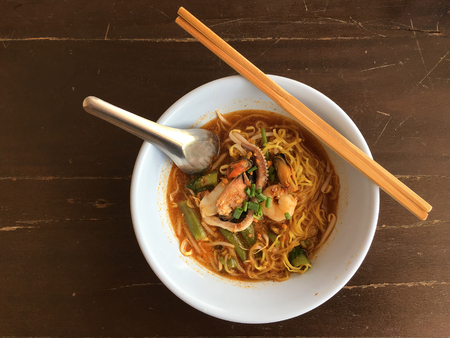 Delicious asian spicy seafood noodle soup with shrimp, squid and shellfish in white bowl on wooden table, Tom Yum Goong. Thai style food. vintage tone color filter.の写真素材