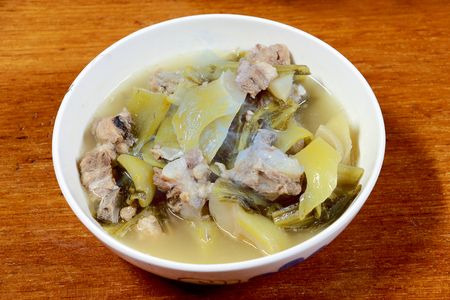 Pickled lettuce soup with spare rips and streaky pork in white blow on wooden table. Thai traditional local northern food.の写真素材