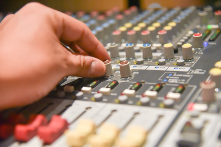 close-up hands of sound engineer adjusting audio mixer controller for live music and studio equipment. This is a quality audio system for professionals. vintage tone & effect light in control room.の写真素材
