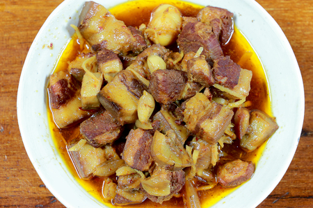 Northern Thailand local dish called Gaaeng Hang Laeh Moo is a Northern Style Hang Lay Curry with Thai herb, streaky pork, pickled onions in a bowl on wooden table. Thai traditional local northern foodの写真素材