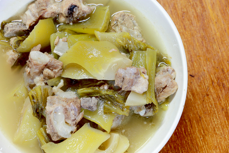 Pickled lettuce soup with spare rips and streaky pork in white blow on wooden table. Thai traditional local northern food.の写真素材