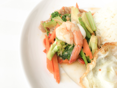 Fried Savory sauteed mixed vegetables with shimp and fried egg served with rice in white dish on white background as Thai homemade meal or recipe in the restaurant. Thai style food.の写真素材