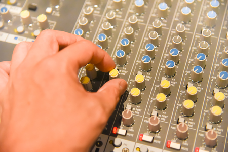 close-up hands of sound engineer adjusting audio mixer controller for live music and studio equipment. This is a quality audio system for professionals. vintage tone & effect light in control room.の写真素材