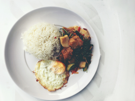 Spicy Stir Fried Fish Fillet with Thai herb with rice and fried egg in white dish on white background. vintage tone color.の写真素材