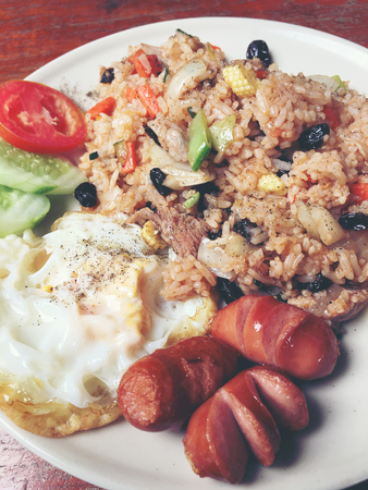 American style breakfast set, fried rice and the style fried egg and sausage in white dish  on wooden table. Thai food. vintage tone color.の写真素材