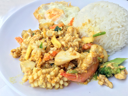 Stir-fried seafood, prawn and squid with yellow curry powder with rice and fried egg in white plate on white background. Thai style food.の写真素材