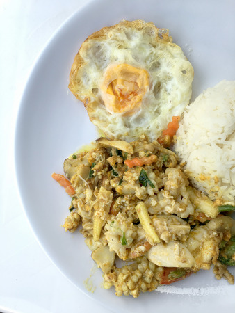 Stir-fried seafood, prawn and squid with yellow curry powder with rice and fried egg in white plate on white background. Thai style food.の写真素材