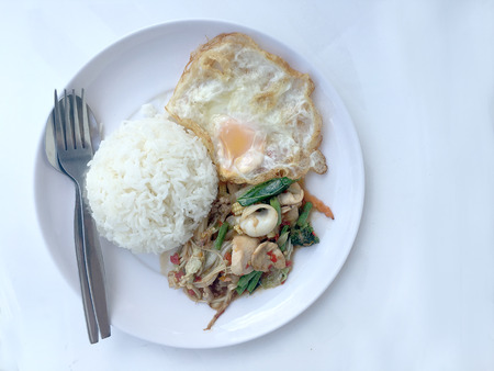 Fried spicy fried seafood with basil leaves and mixed vegetable and fried egg on jasmine rice in white dish. Thai style food.の写真素材