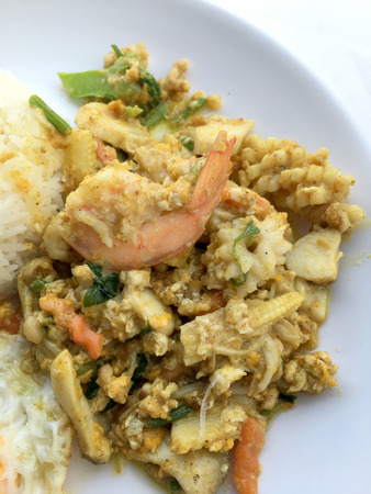 Stir-fried seafood, prawn and squid with yellow curry powder with rice and fried egg in white plate on white background. Thai style food.の写真素材