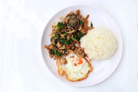 Stir-fried basil leave with minced pork, chicken, fried preserved egg and carrot, yellow corn, Broccoli with rice and fried egg in white dish on white background. Thai style food.の写真素材