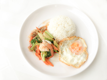 Fried Savory sauteed mixed vegetables with shimp and fried egg served with rice in white dish on white background as Thai homemade meal or recipe in the restaurant. Thai style food.の写真素材
