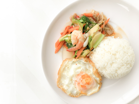 Fried Savory sauteed mixed vegetables with shimp and fried egg served with rice in white dish on white background as Thai homemade meal or recipe in the restaurant. Thai style food.の写真素材