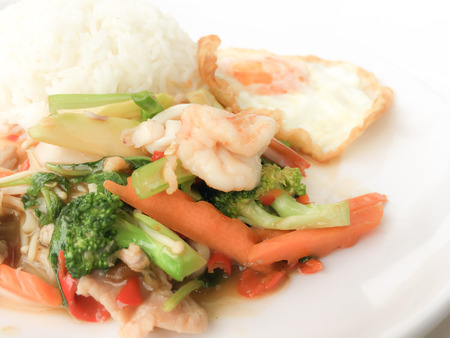 Fried Savory sauteed mixed vegetables with shimp and fried egg served with rice in white dish on white background as Thai homemade meal or recipe in the restaurant. Thai style food.の写真素材