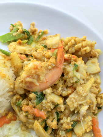 Stir-fried seafood, prawn and squid with yellow curry powder with rice and fried egg in white plate on white background. Thai style food.の写真素材