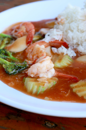 stir fried shrimp and Broccoli in thai red curry paste sauce with rice, Curry fried shrimps and cooked rice in white dish closeup on wooden table. Thai style food.の写真素材