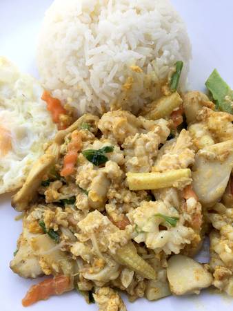 Stir-fried seafood, prawn and squid with yellow curry powder with rice and fried egg in white plate on white background. Thai style food.の写真素材