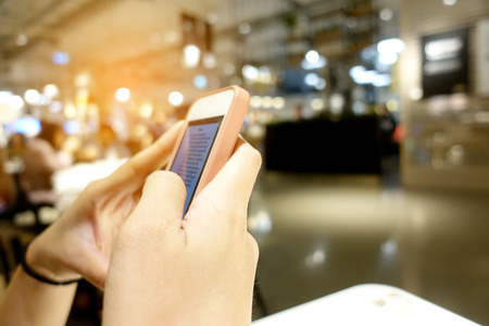 Close up of women's hands with a pink nails holding cell telephone, hipster girl watching video and texting a message to her family on mobile phone during coffee break in restaurantsの写真素材