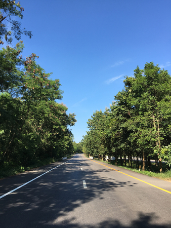 Beautiful local asphalt road way to the natural in rainy season with trees forest, blue sky and mountains in the backgrounds in the north of Thailand.の写真素材