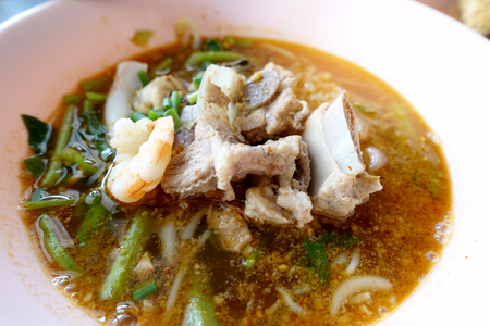 Spicy seafood noodles soup with pork bone crayfish, shrimp.  Asia food in pink bowl on wooden table background. Thai style noodle and street food of Thailand.   top viewの写真素材