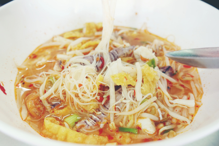 Spicy seafood noodles soup with crayfish, shrimp and mushroom. Asia food in white bowl on table background. Thai style noodle and street food of Thailand.の写真素材
