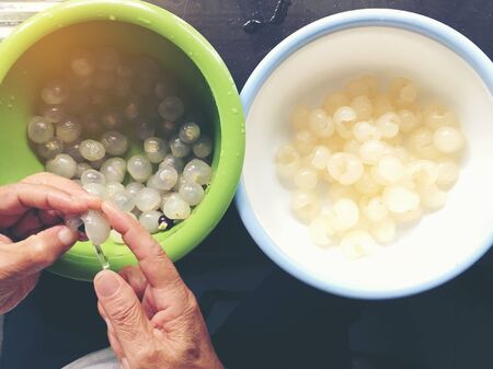 Hand of woman is fresh peel longan fruit or dimocarpus longan from small knife for remove skin from longan bark in a blow at the kitchen. Thai and Exotic fruit. Cooking Conceptの写真素材