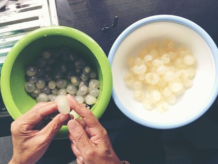Hand of woman is fresh peel longan fruit or dimocarpus longan from small knife for remove skin from longan bark in a blow at the kitchen. Thai and Exotic fruit. Cooking Conceptの写真素材