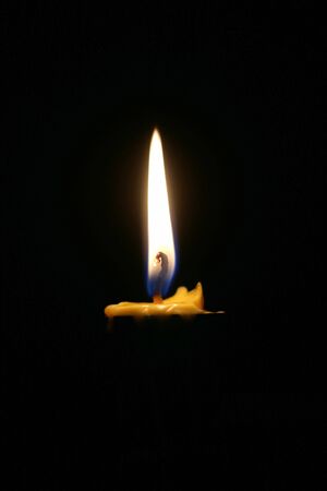 One or Single yellow light candle burning brightly in the black background, candle light isolated black in dark night.の写真素材