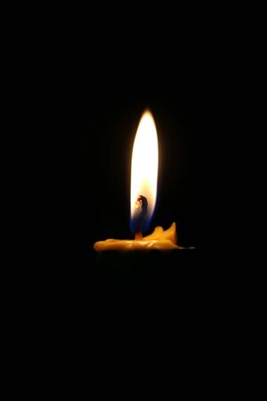 One or Single yellow light candle burning brightly in the black background, candle light isolated black in dark night.の写真素材