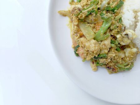 Stir fry mixed-seafood with with yellow curry powderin thai style with fried egg and rice in in white plate on white background.の写真素材