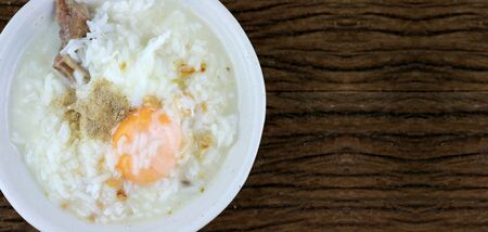 Homemade Thai Rice Soup With chicken, pork and Soft boiled egg or onsen egg in white blow on rustic wooden background. Thai style Food. Top view.の写真素材