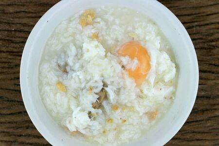 Homemade Thai Rice Soup With chicken, pork and Soft boiled egg or onsen egg in white blow on rustic wooden background. Thai style Food. Top view.の写真素材