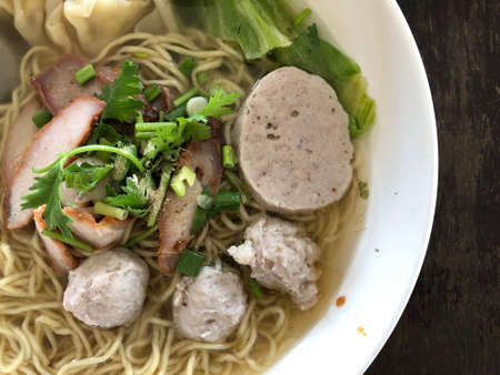 Thai noodle soup wonton roasted pork / yellow egg noodle with pork dumpling and chinese cabbage vegetable in soup bowl on wooden table top view. Thai style food.の写真素材