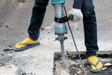 Male workers use electric concrete breaker for digging and drilling concrete repairing driveway surface with jackhammer at the local city road, during sidewalk, work construction site.の写真素材