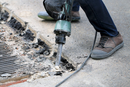 Male workers use electric concrete breaker for digging and drilling concrete repairing driveway surface with jackhammer at the local city road, during sidewalk, work construction site.の写真素材