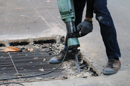 Male workers use electric concrete breaker for digging and drilling concrete repairing driveway surface with jackhammer at the local city road, during sidewalk, work construction site.の写真素材