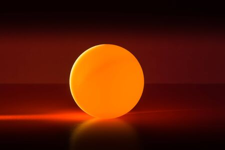 Yellow ball on a red dark background illuminated by a side beam of light, abstract backgroundの写真素材