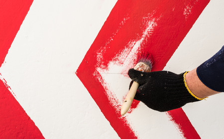 The hand in the black glove holds the brush. On the wall with red paint draws an arrow