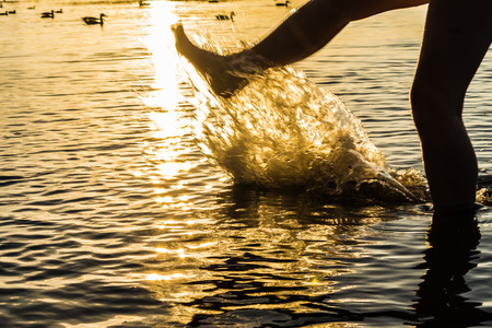 A splash of water created by the boy's foot, the orange trace of the scorching sun, summer sunset backgroundの写真素材