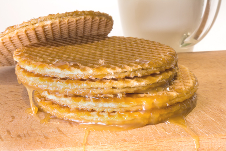 Round cookies or wafers with a layer of caramel lies on a rough pile on a wooden board, mug of clear glass with milk, food close-up abstract backgroundの写真素材