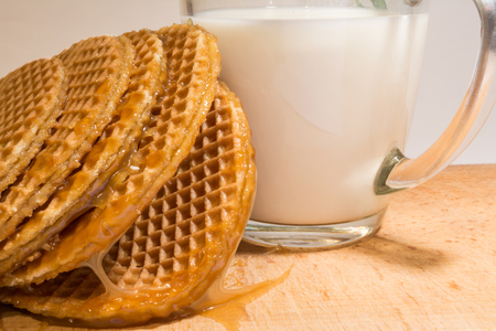 Round cookies or wafers with a layer of caramel lies on a rough pile on a wooden board, mug of clear glass with milk, food close-up abstract backgroundの写真素材
