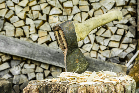 old ax is stuck in a stump against the backdrop of a woodpile, selective focus, close-up abstract backgroundの写真素材