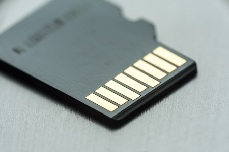 black micro sd card with gold contacts on a gray metallic surface, selective focus, macro