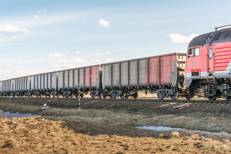 locomotive and a lot of freight cars are traveling by rail, freight train on rails in the steppe, spring sunny day with clear skyの写真素材