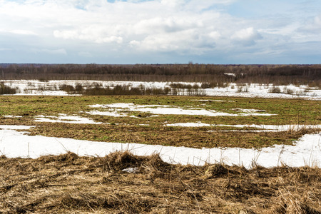 The melting of the snow on the fields in early spring, sunny day with blue sky and clouds, beautiful nature backgroundの写真素材
