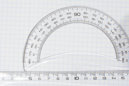 transparent plastic protractor, triangle and ruler on the background of a notebook in a cageの写真素材