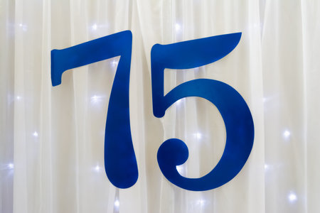 Blue inscription 75 on a background of white fabric and shimmering garland. Cover for the...