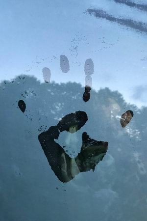 Palm print on the fogged glass of a car. The forest and the sky are reflected on the wet glass....