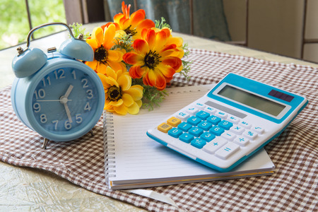 note paper  with calculator and flower and clock on table.の写真素材